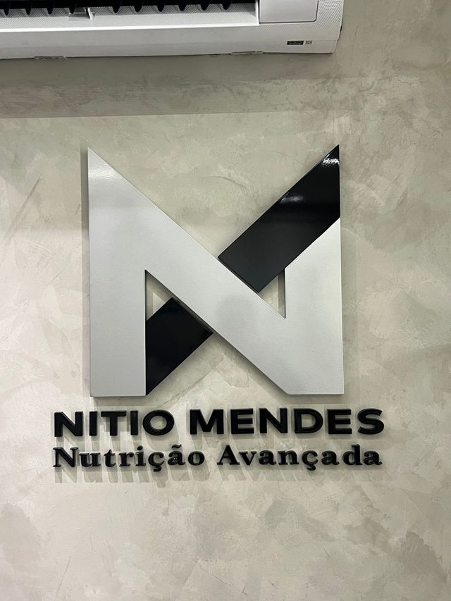 Monograma N em prata e preto, com o nome Nítio Mendes Nutrição Avançada, na parede de cimento queimado