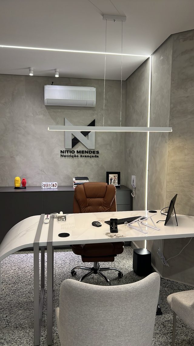 Sala de atendimento com mesa de mármore, iluminação linear de LED e o monograma Nítio Mendes na parede