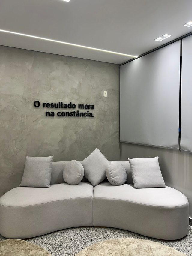 Sala de espera do consultório com sofá cinza e, na parede de cimento queimado, a frase “O resultado mora na constância.”