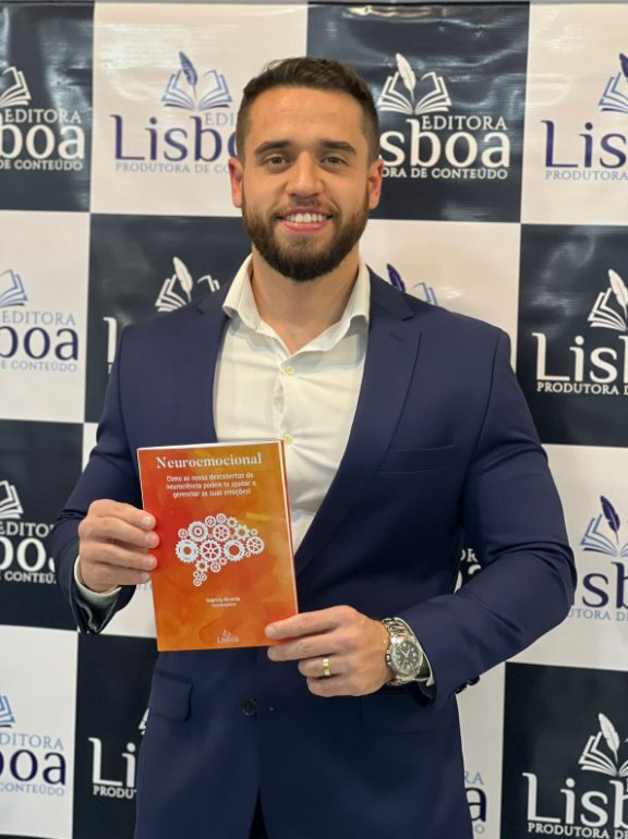 Nítio Mendes segurando o livro Neuroemocional diante do painel da Editora Lisboa